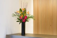 red and orange flowers in tall black vase on reception desk