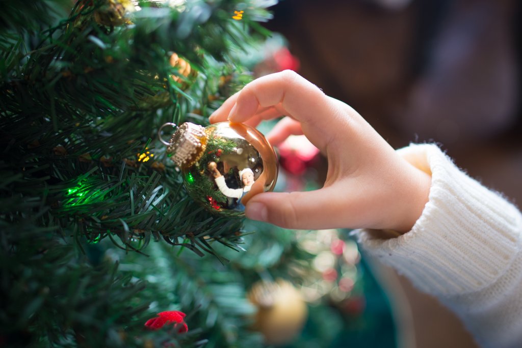 Close up of an arm in a white woollen jumper putting a gold bauble onto a christmas tree