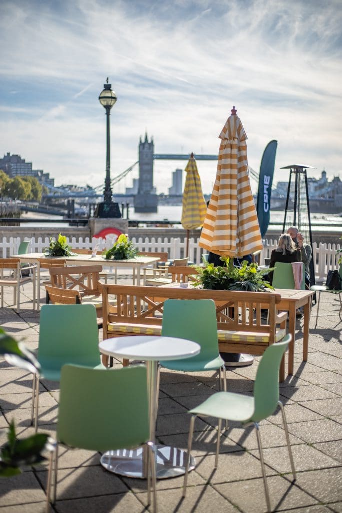 Outdoor cbre terrace with striped parasol, tables, and lush plant displays.